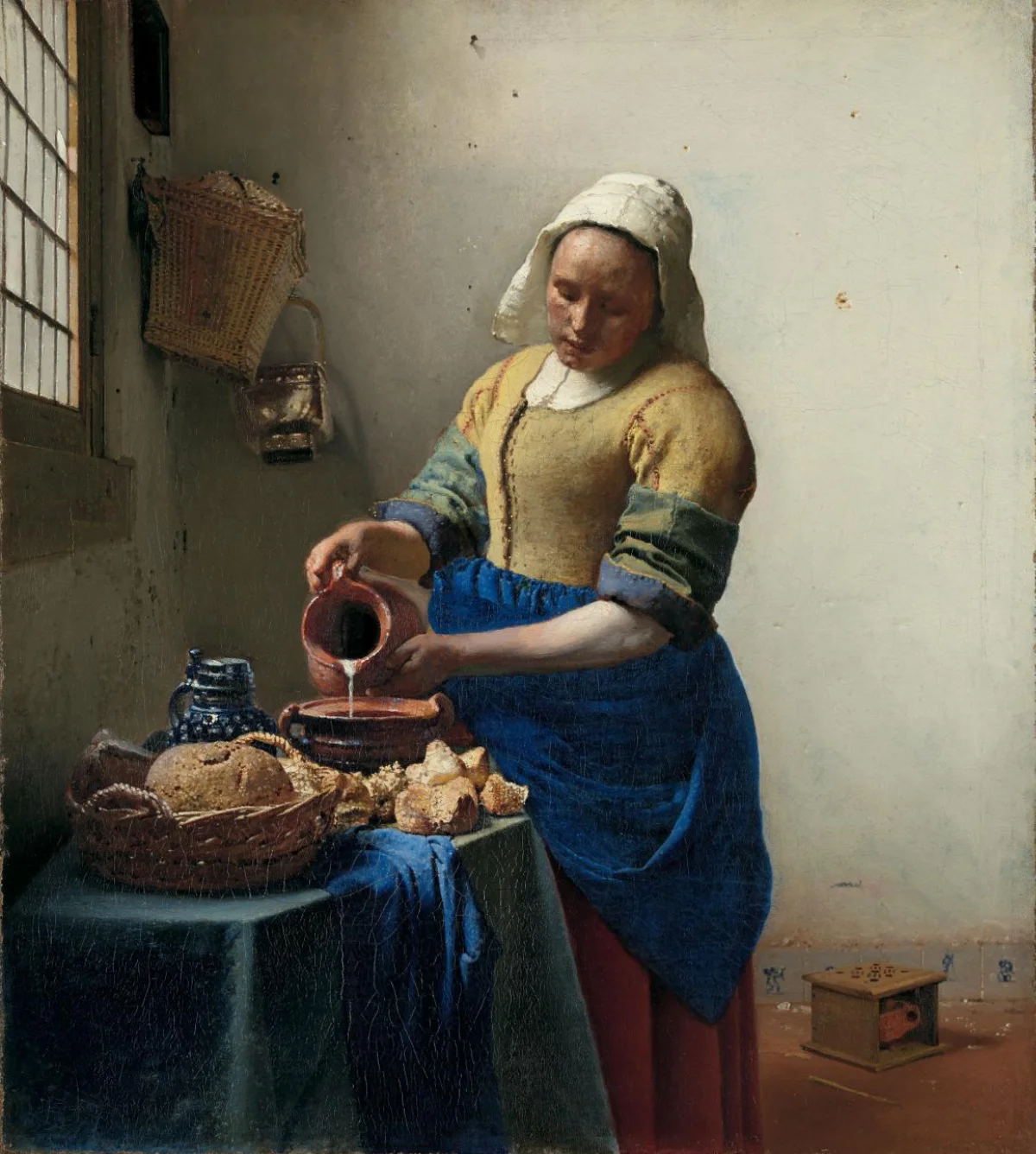 Vermeer painting of a kitchen maid pouring milk beside bread, wearing a yellow bodice and blue apron in window light.